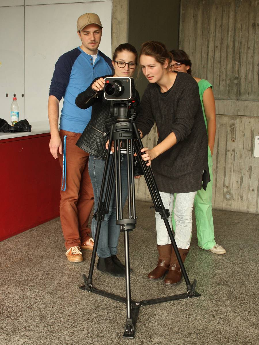 Vier Studenten stehen vor einer Kamera auf einem Stativ und schauen sie sich genauer an.